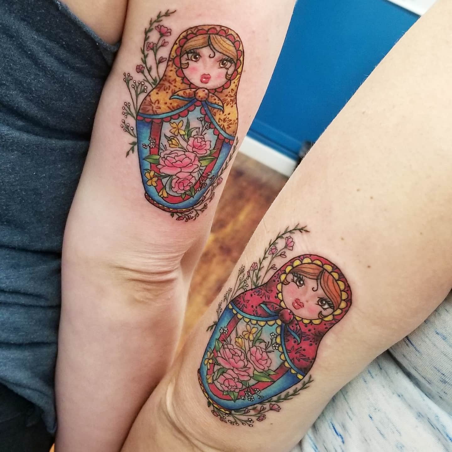 Two arms with colorful, matching Matryoshka doll tattoos featuring floral designs